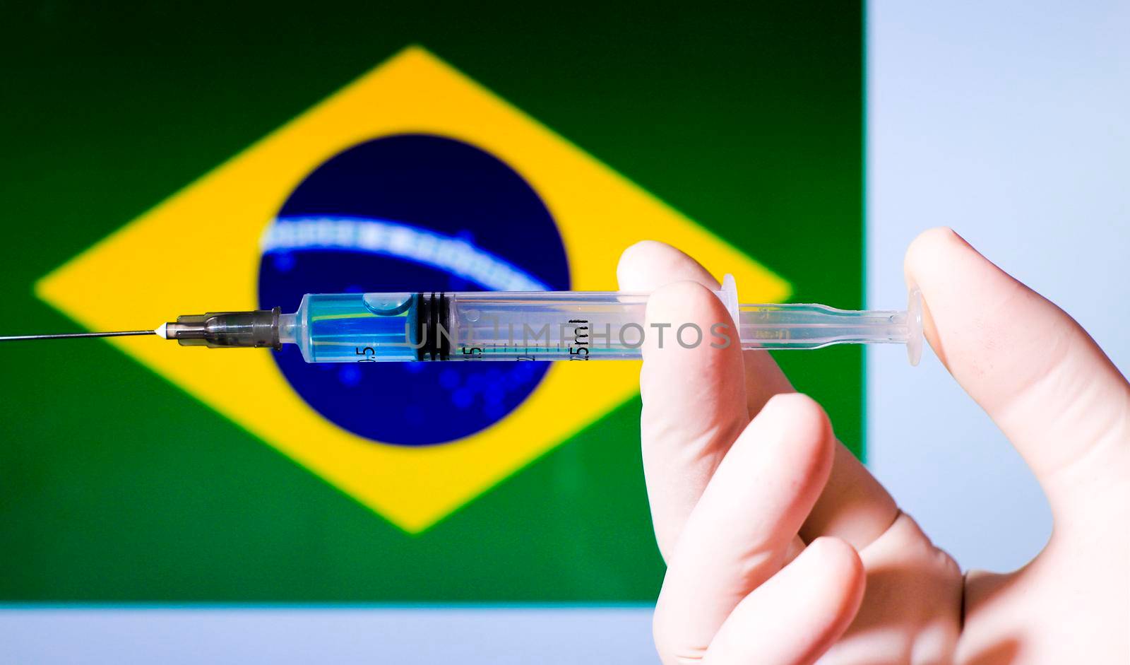 Hand in surgery glove holding syringe with covid vaccine. Brazilian flag in the background