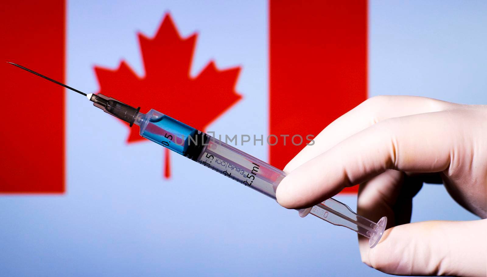 Hand in surgery glove holding syringe with covid vaccine. Canadian flag in the background