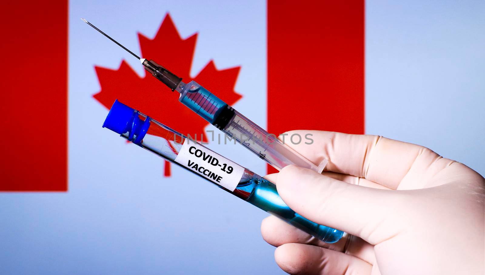 Hand in surgery glove holding syringe with covid vaccine. Canadian flag in the background