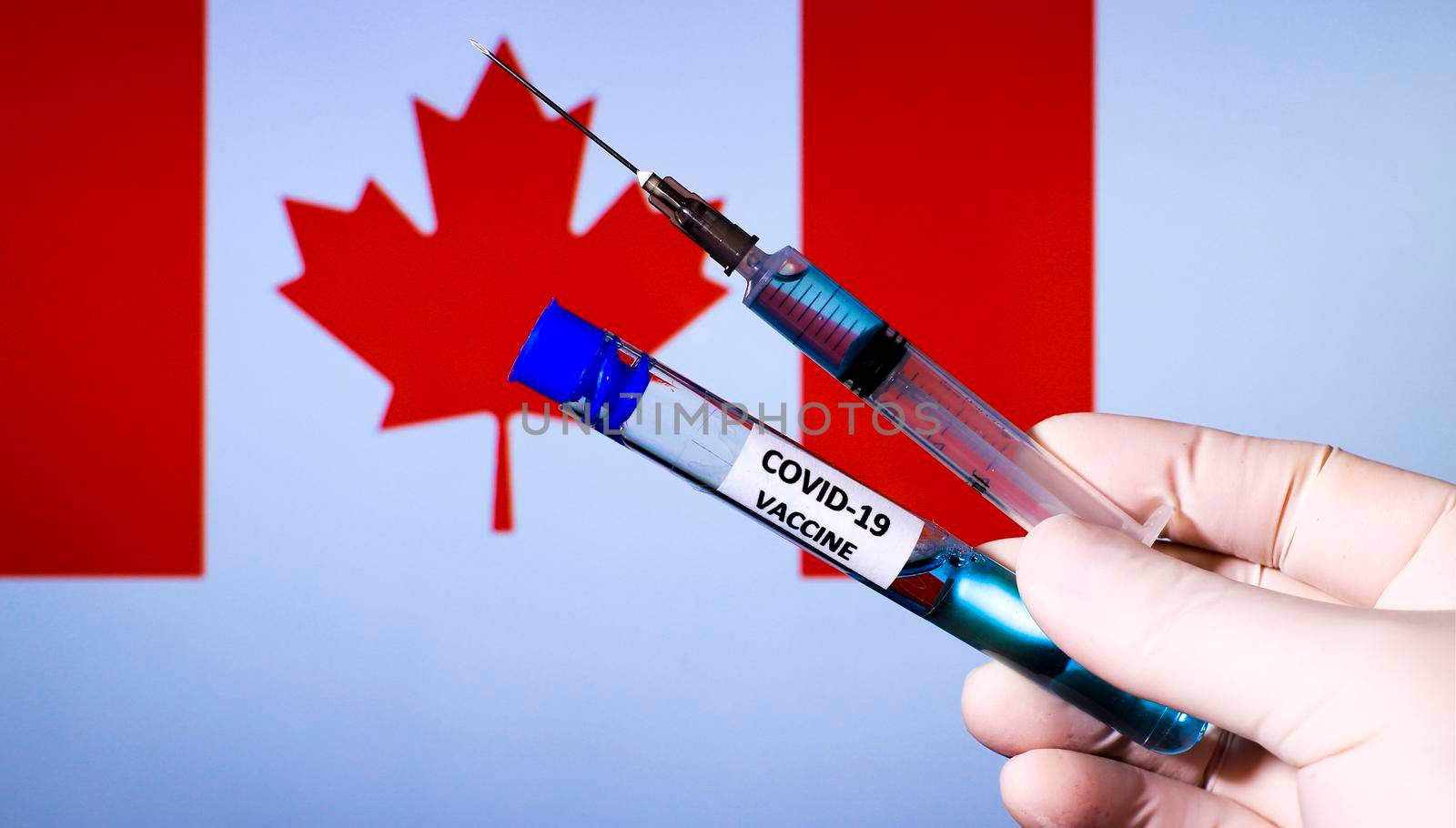 Hand in surgery glove holding syringe with covid vaccine. Canadian flag in the background