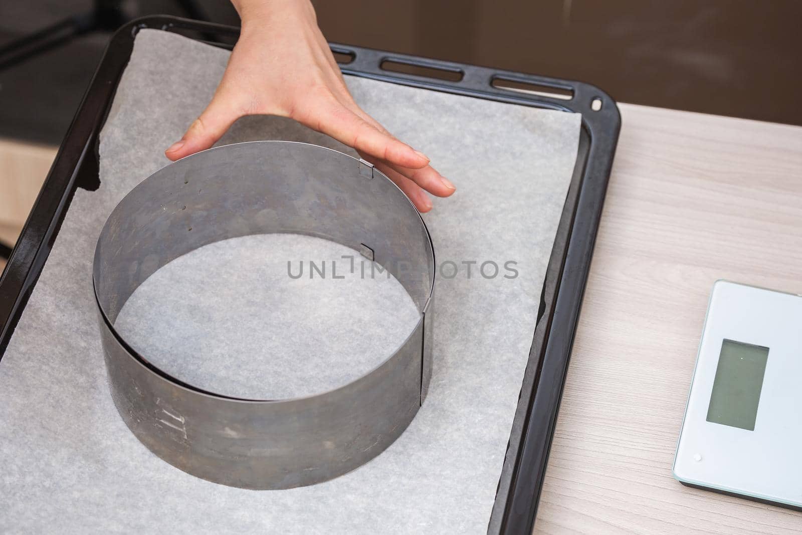 Hand holds iron cake form on baking paper on a tray. Preparing homemade cake.