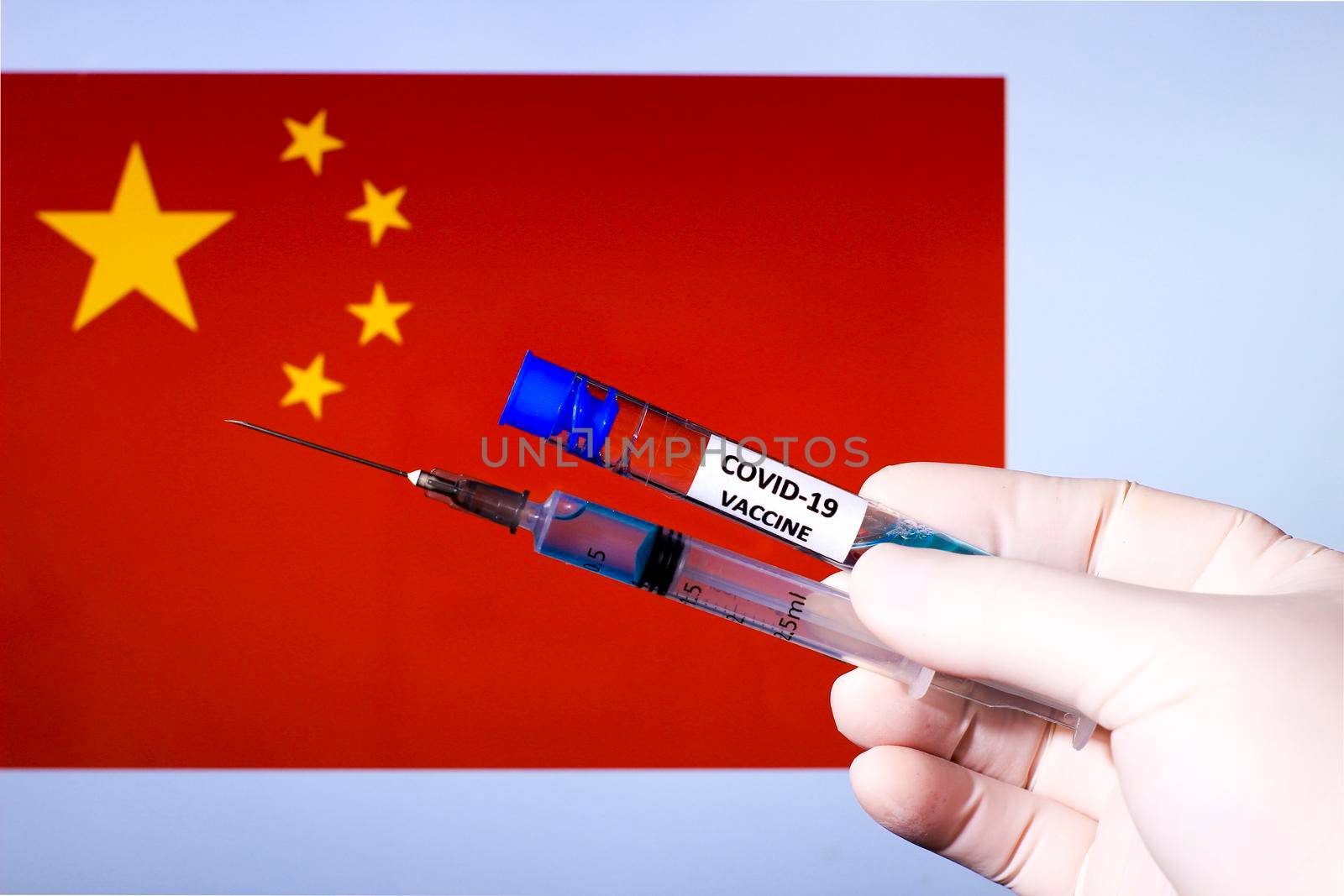 Hand in surgery glove holding syringe with covid vaccine. China flag in the background