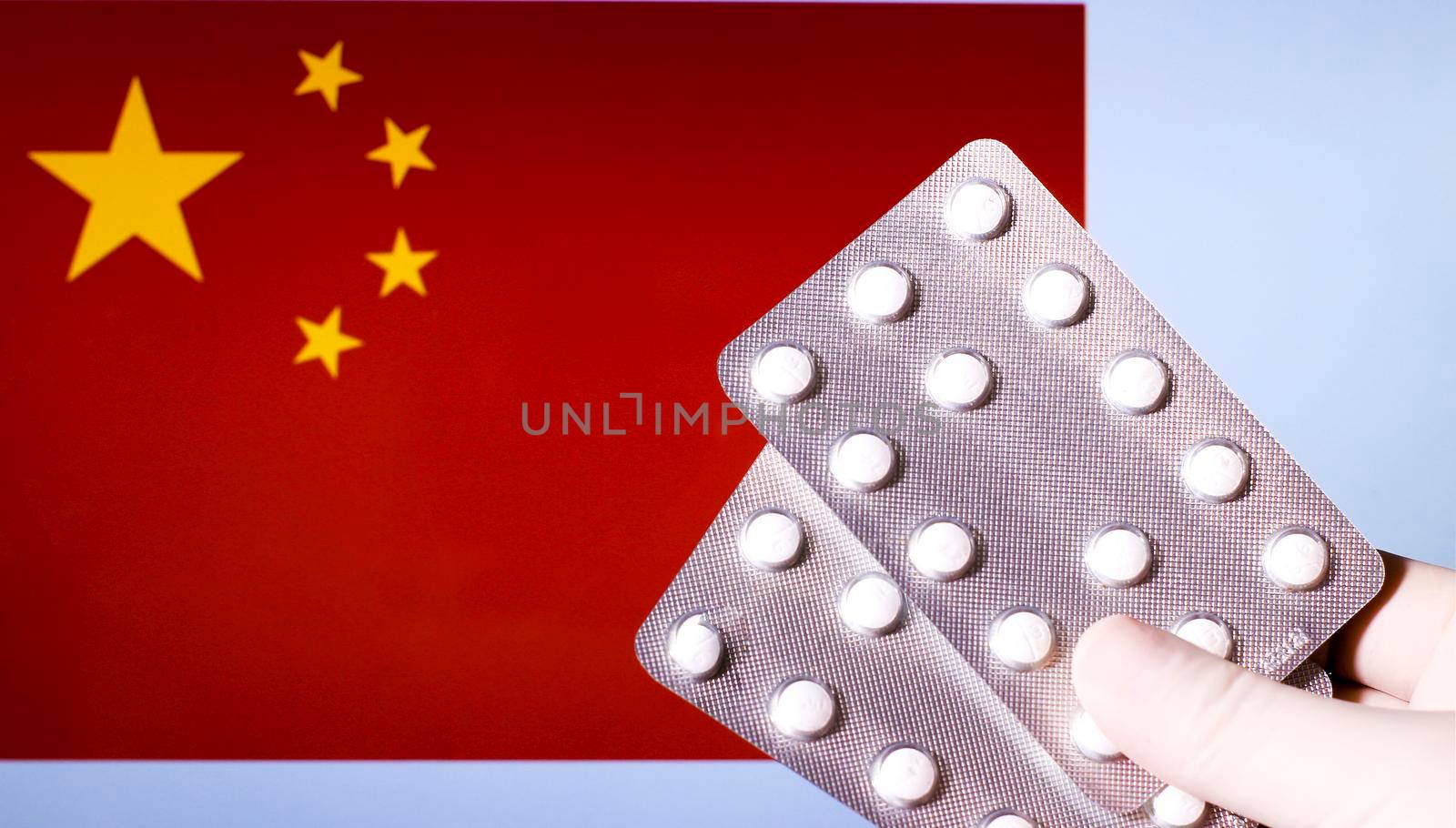 Hand in surgical glove holding pill blisters. China flag in the background
