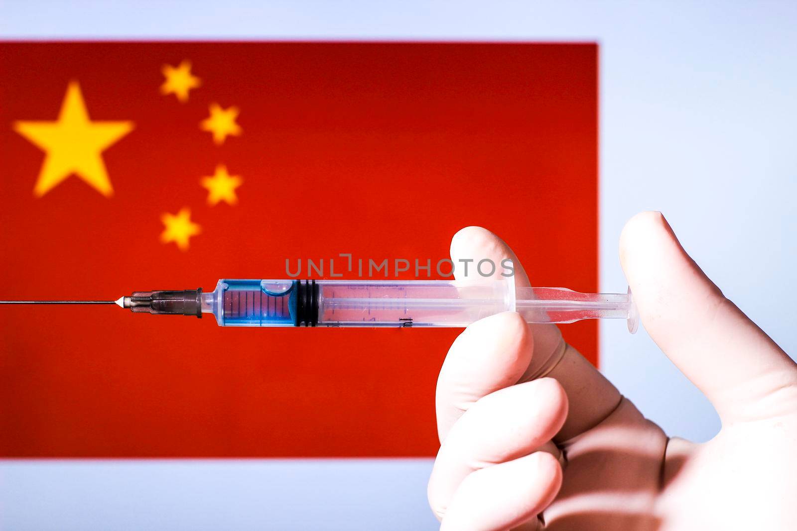 Hand in surgery glove holding syringe with covid vaccine. China flag in the background