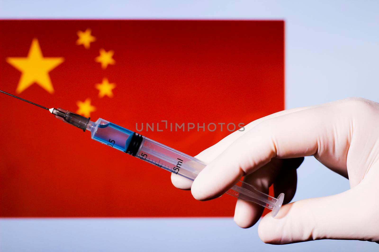 Hand in surgery glove holding syringe with covid vaccine. China flag in the background