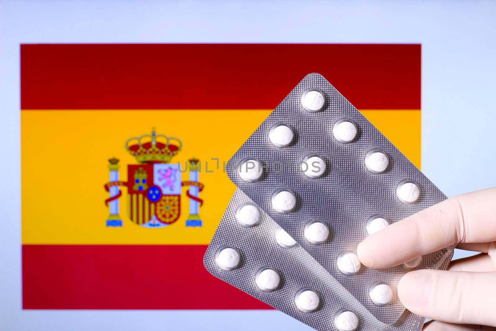 Hand in surgical glove holding pill blisters. Spanish flag in the background