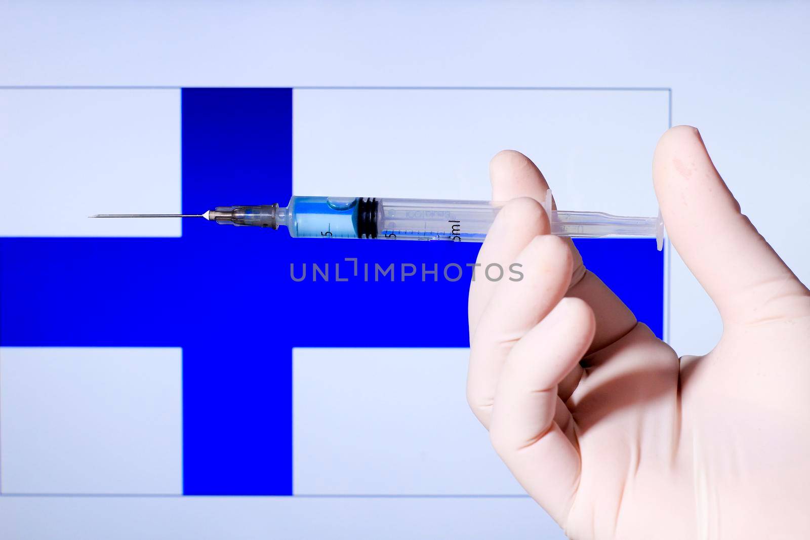 Hand in surgery glove holding syringe with covid vaccine. Finnish flag in the background