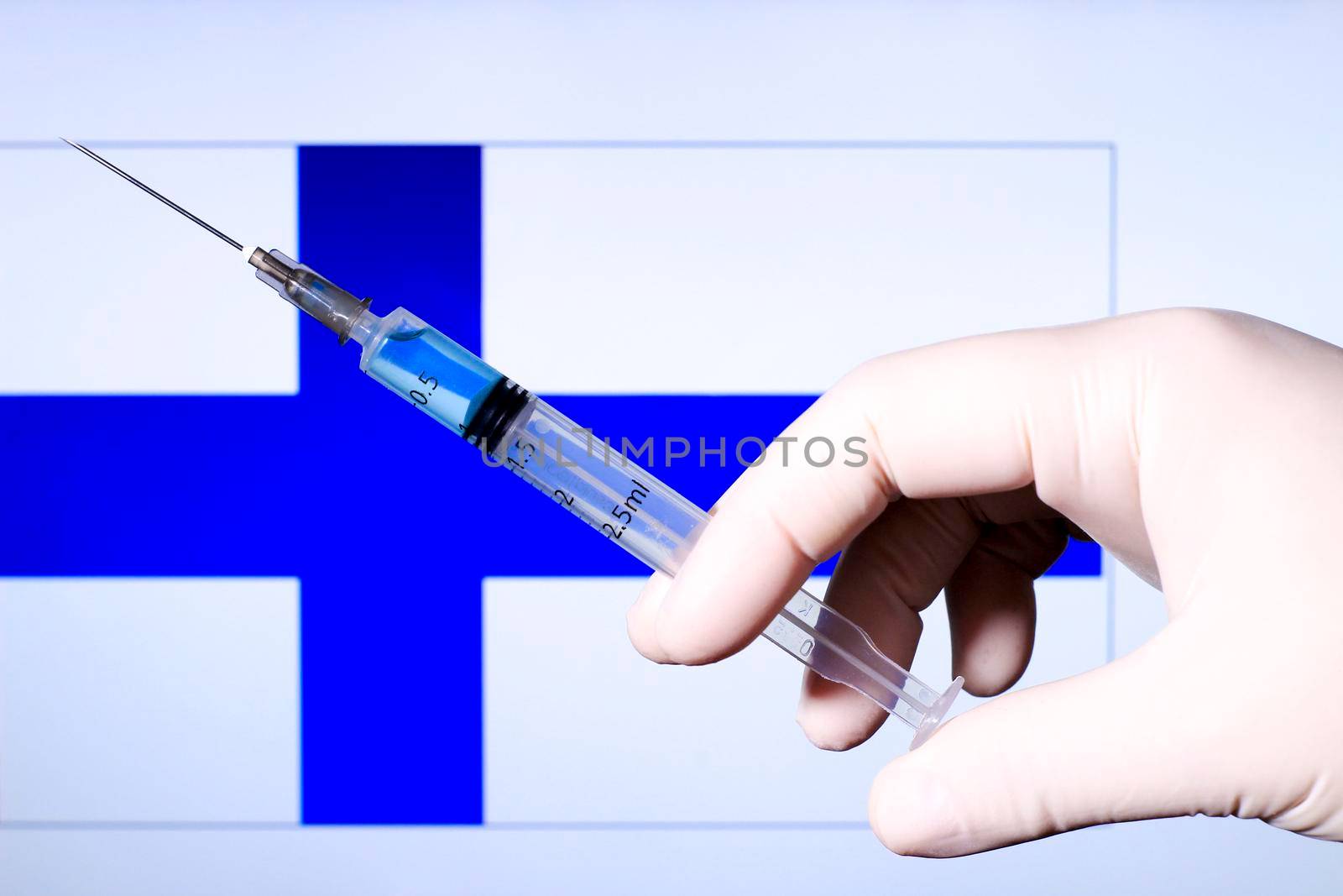 Hand in surgery glove holding syringe with covid vaccine. Finnish flag in the background