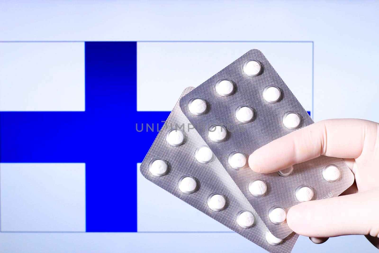 Hand in surgical glove holding pill blisters. Finnish flag in the background
