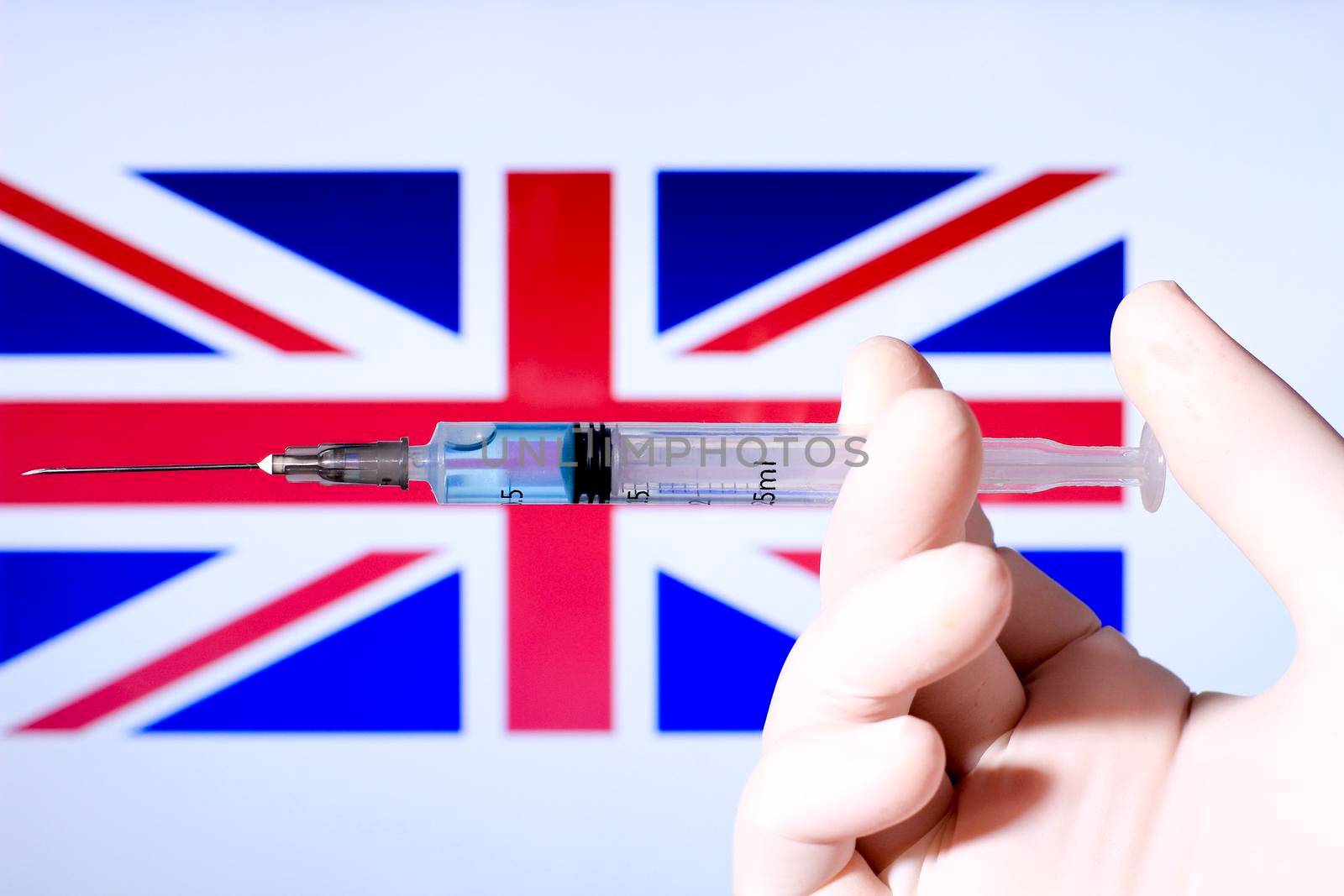 Hand in surgery glove holding syringe with covid vaccine. British flag in the background
