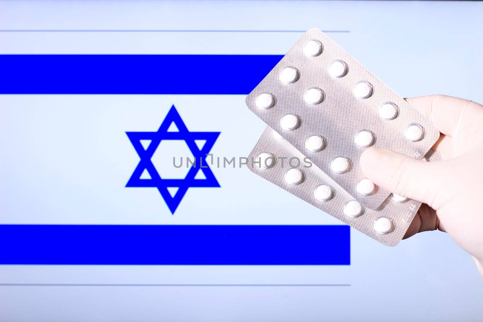 Hand in surgical glove holding pill blisters. Israeli flag in the background
