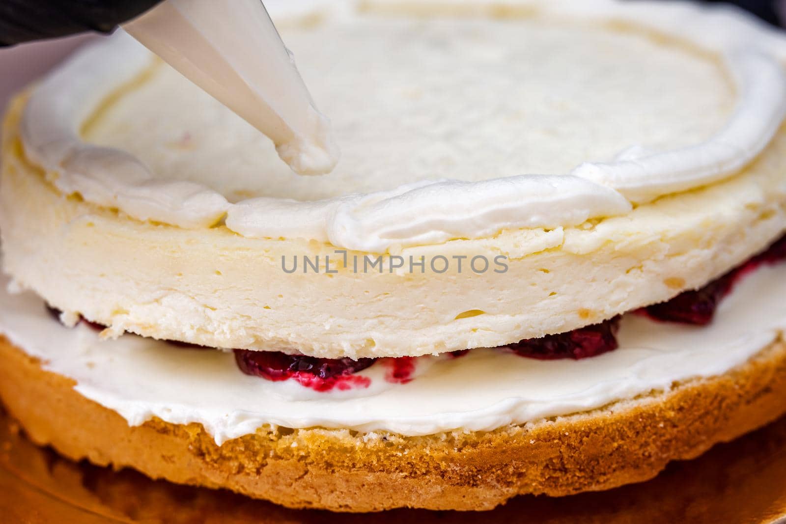 Female hand in black glove squeezes out cream on a cheesecake with coconut.