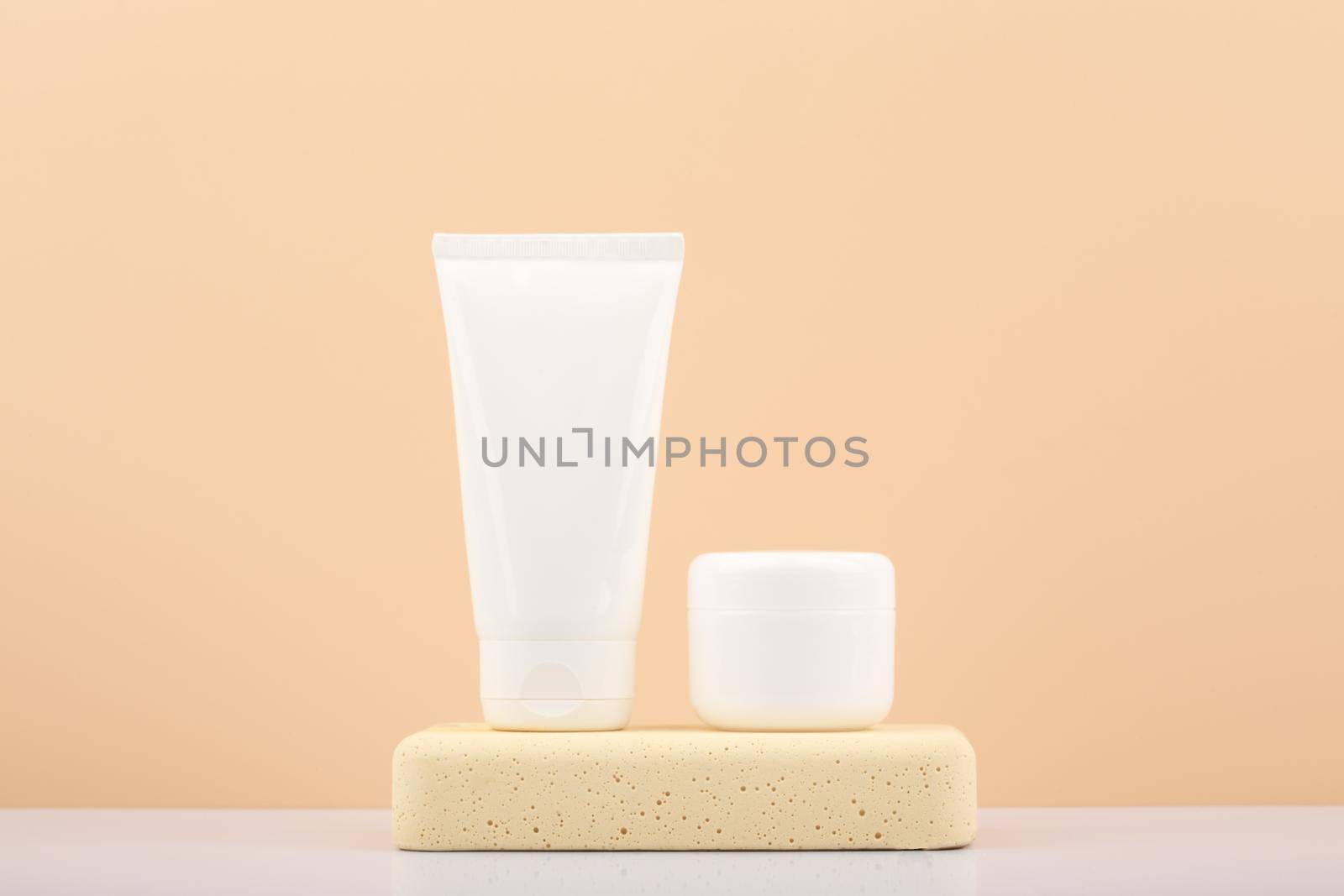 White cream tubes with cosmetic products on beige stone podium against beige background with copy space. Concept of natural cosmetics and daily skin care routine