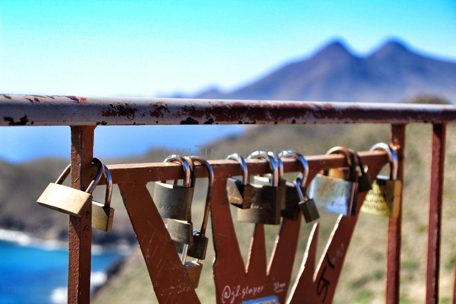 Almeria, Spain- September 23, 2018: Romantic Padlocks in the morning on a fence in Cabo de Gata. Volcanic mountains in the background.