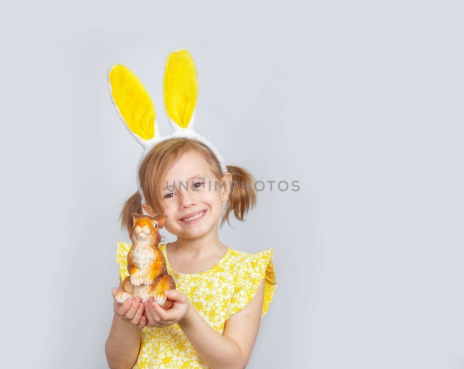 Little Caucasian girl posing on plain background in yellow dress and bunny ears by galinasharapova