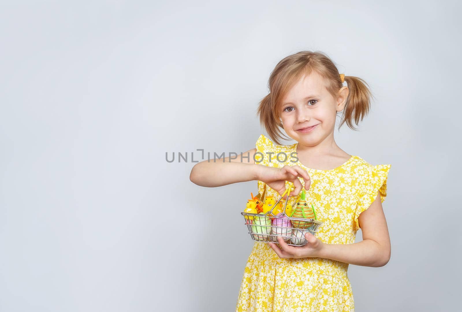 Portrait of a little cute Caucasian smiling girl with a shopping basket filled with Easter decorations. Easter background with place to insert text.