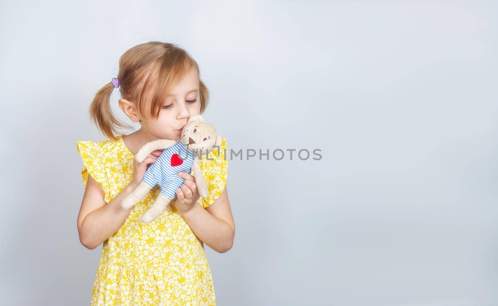 Little Caucasian girl with teddy bear kissing her toy bear, advertisement posing against studio wall. Advertising concept
