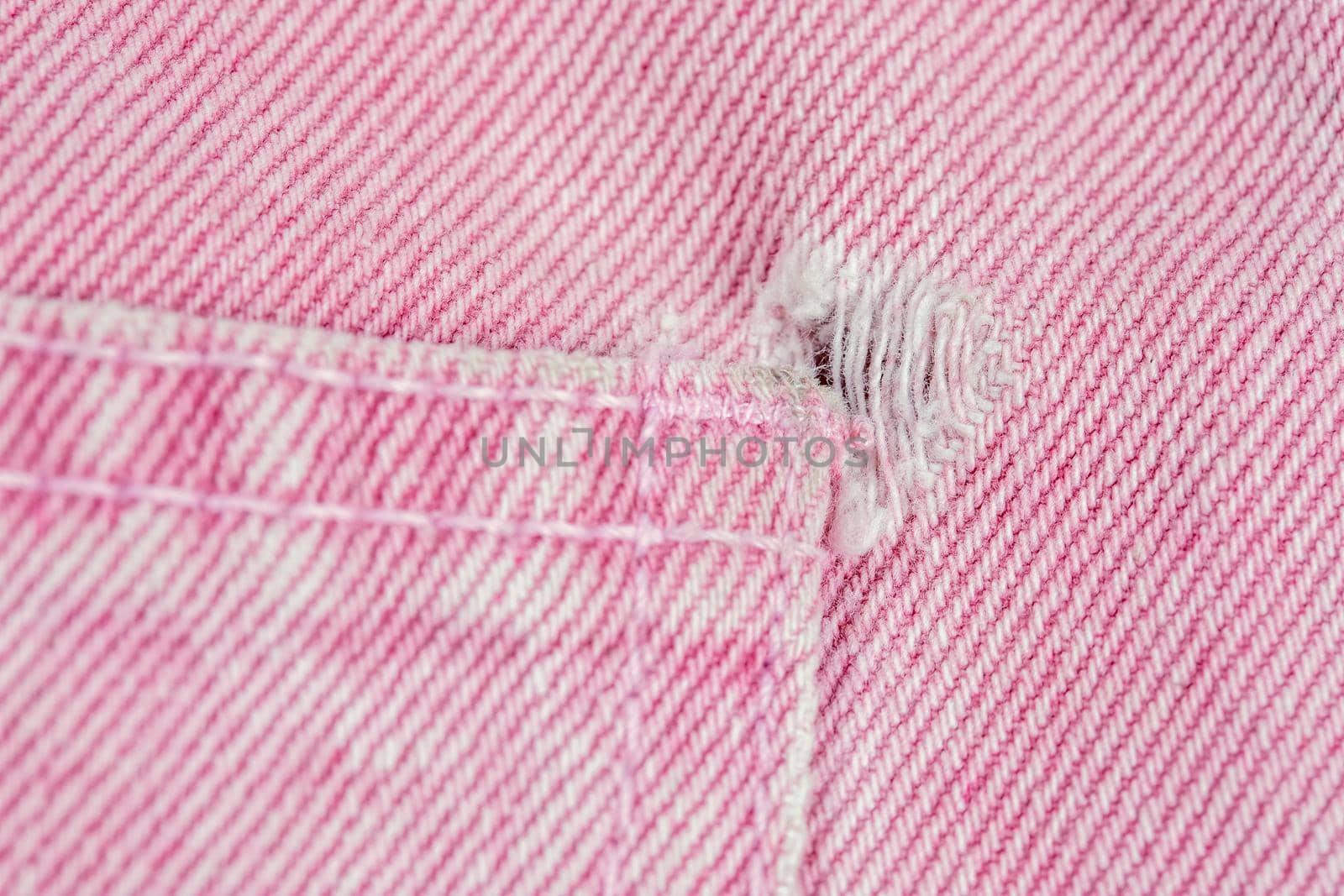 A close-up of a frayed pink jeans pocket, a torn off pocket.