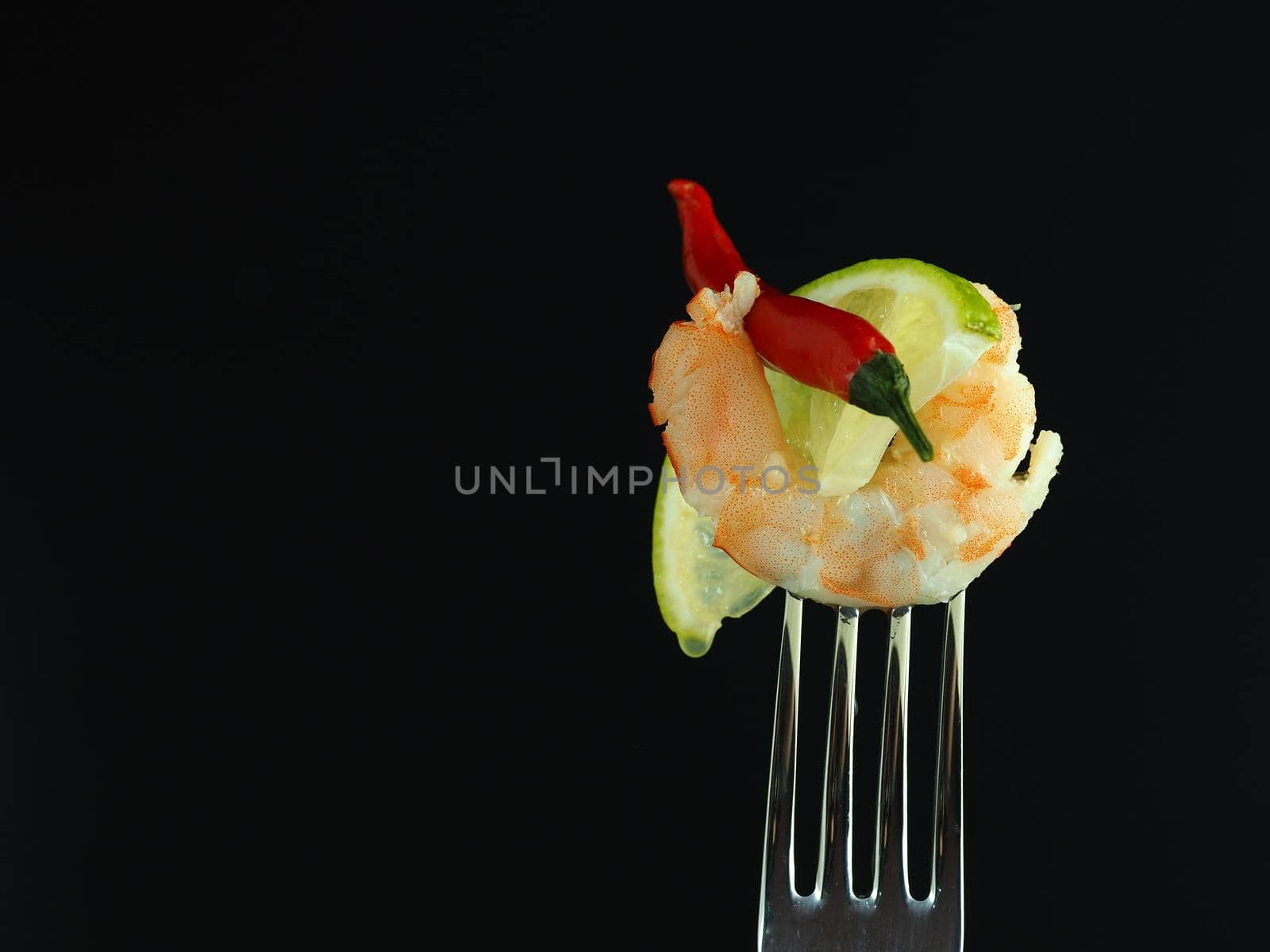 Boiled shrimp on a fork with a piece of lime, isolated on a black background. High quality photo