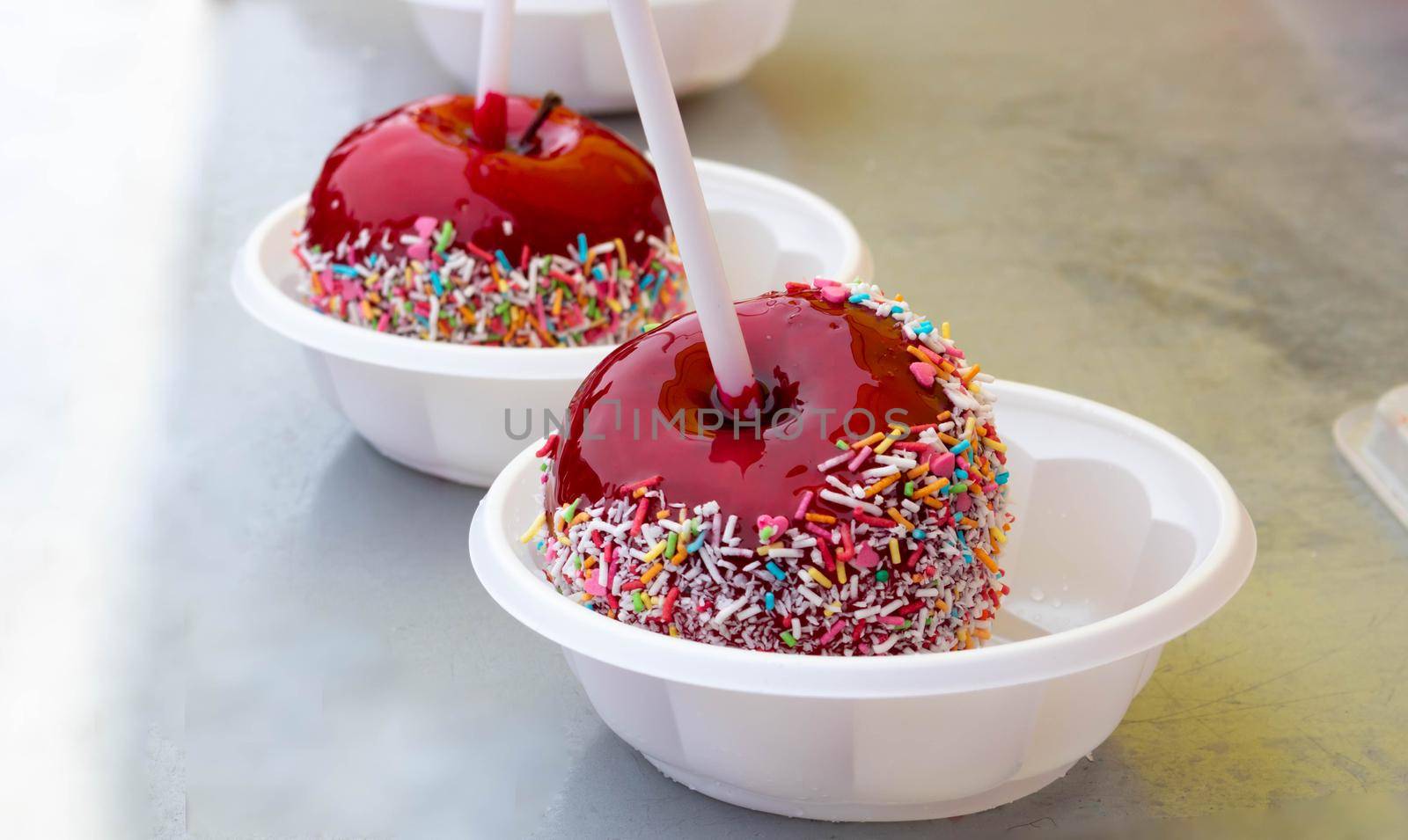 A red caramelized apple on a stick, covered in hard red sugar, standing in a plastic plate to serve as a festive treat. The concept of Easter, Maslenitsa,Valentine's Day.