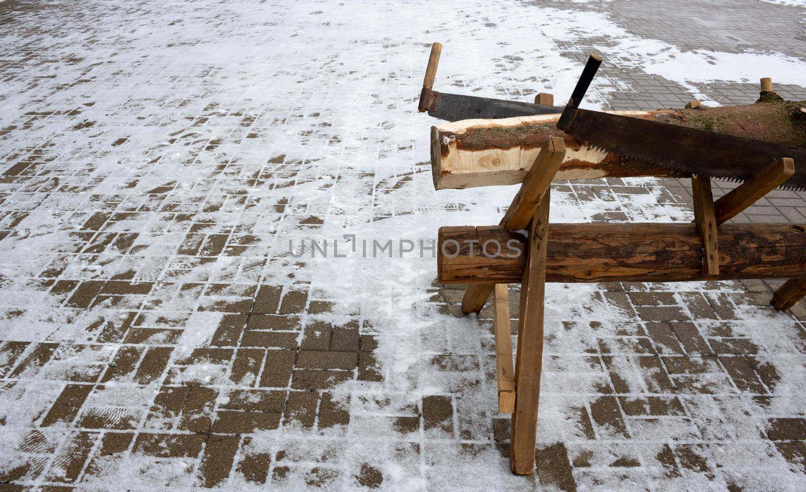 A wooden trestle with a coniferous log and two hand saws on it. Space for text.