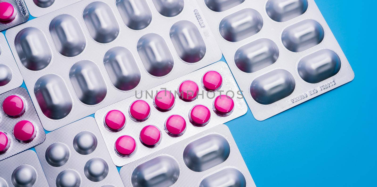 Pink tablets in blister pack and silver aluminium foil pack for capsule and tablets pills in pharmaceutical industry. Pharmaceutical package manufacturing. Top view of round tablets pills. Pharmacy.