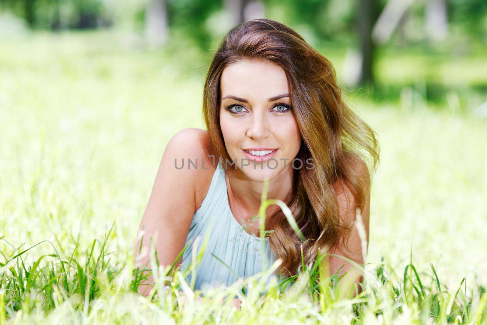 Beautiful young woman in blue dress lying on grass