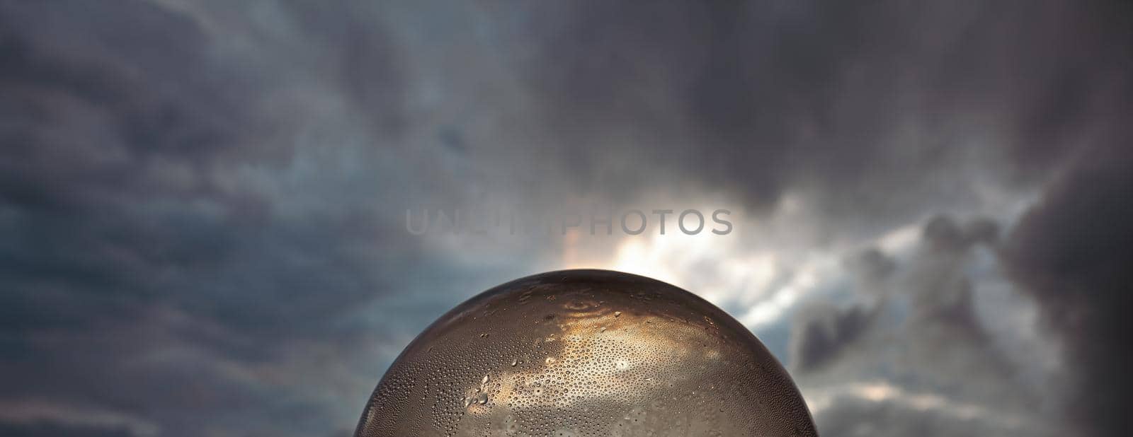 Abstract background. Glass ball with water drops against dramatic sunset sky