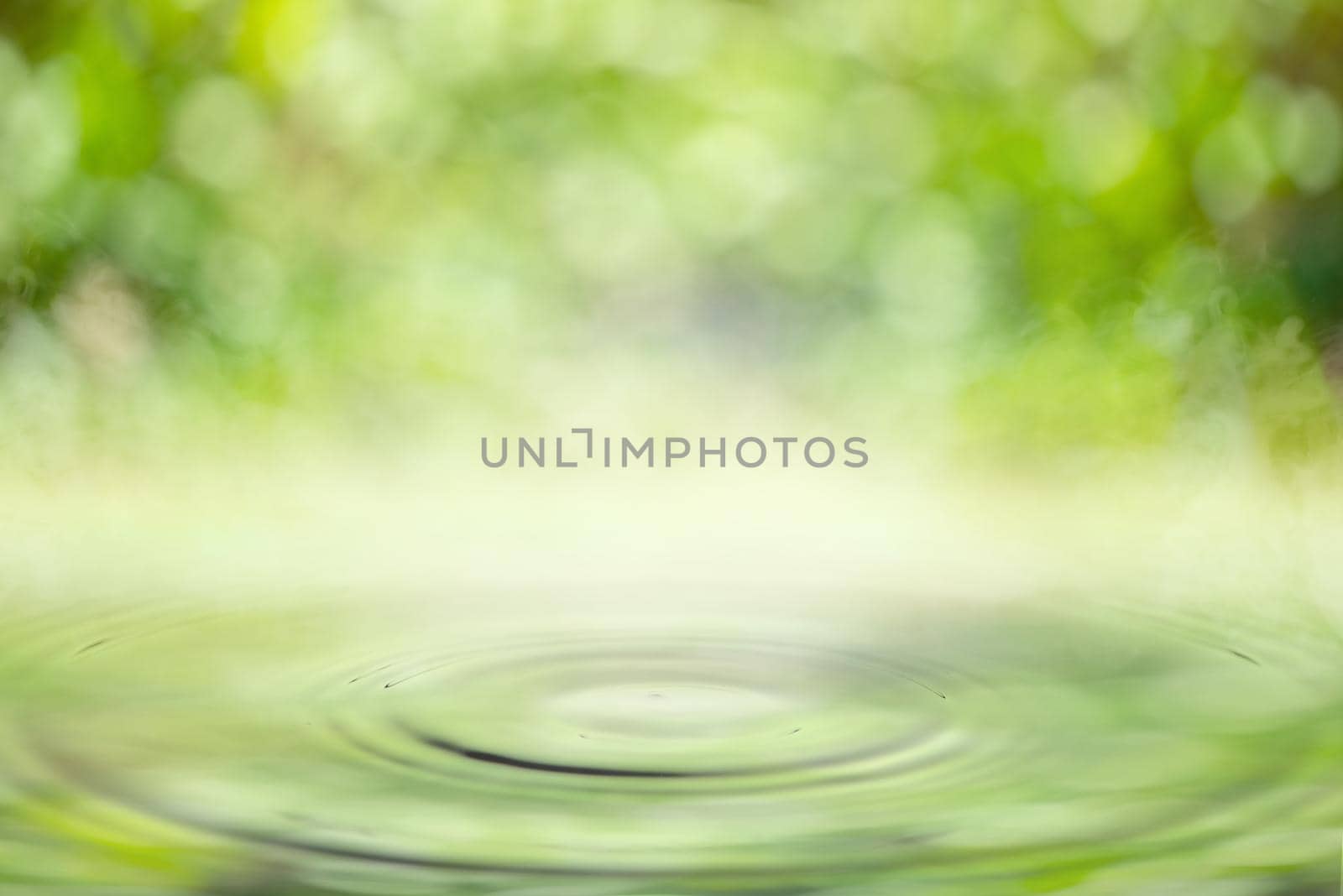 Drop falling in water with ripples with light green bokeh background.