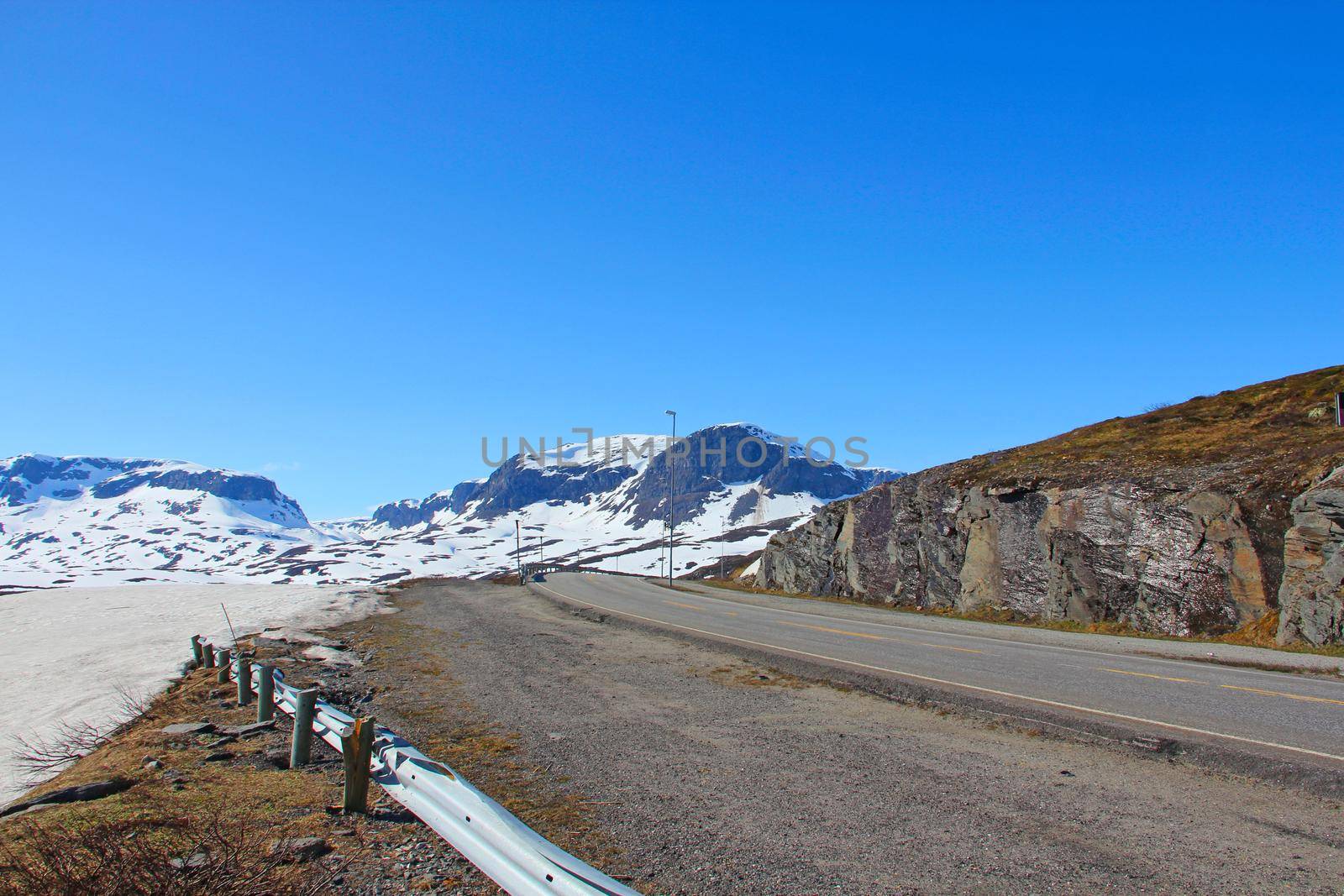 Highland mountain valley with melting snow under clear blue sky, view on road,beautiful arctic polar Norway landscape