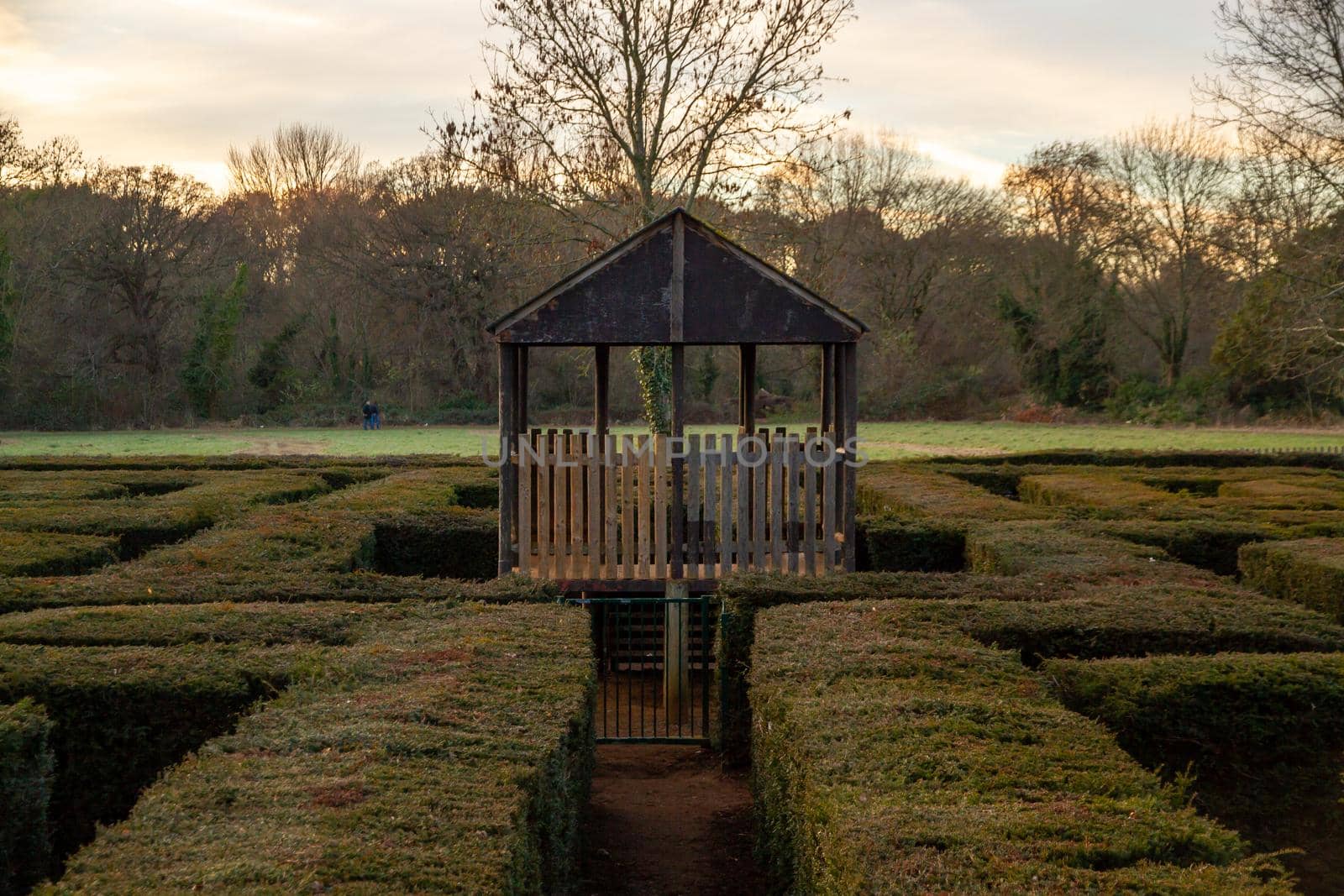 A wood cabin inside a maze in a park at sunset