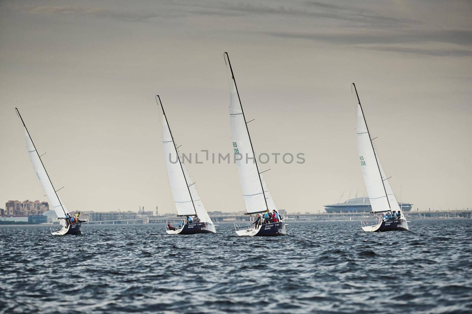 Russia, St.Petersburg, 05 September 2020: Some sailboats in a list goes by sea, the storm sky, regatta, Gazprom arena stadium on background. High quality photo