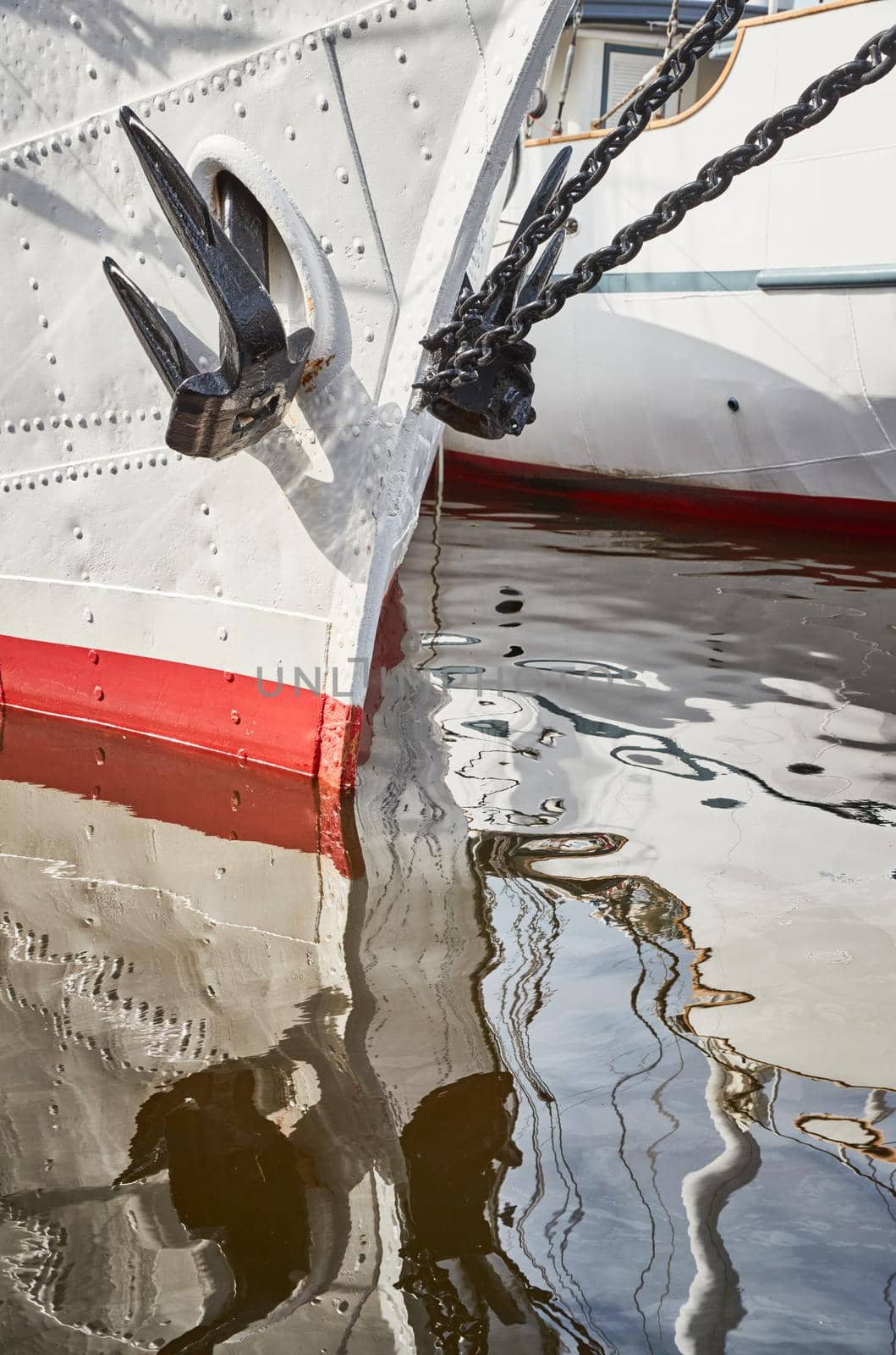 Nasal part of a sailing frigate of white color with an anchor on a nose, bright reflection in water. High quality photo