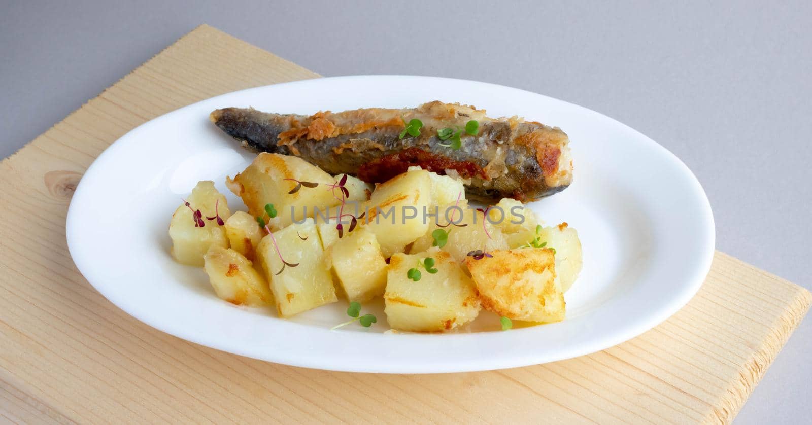 Fried fish and potatoes on a white plate on the table.
