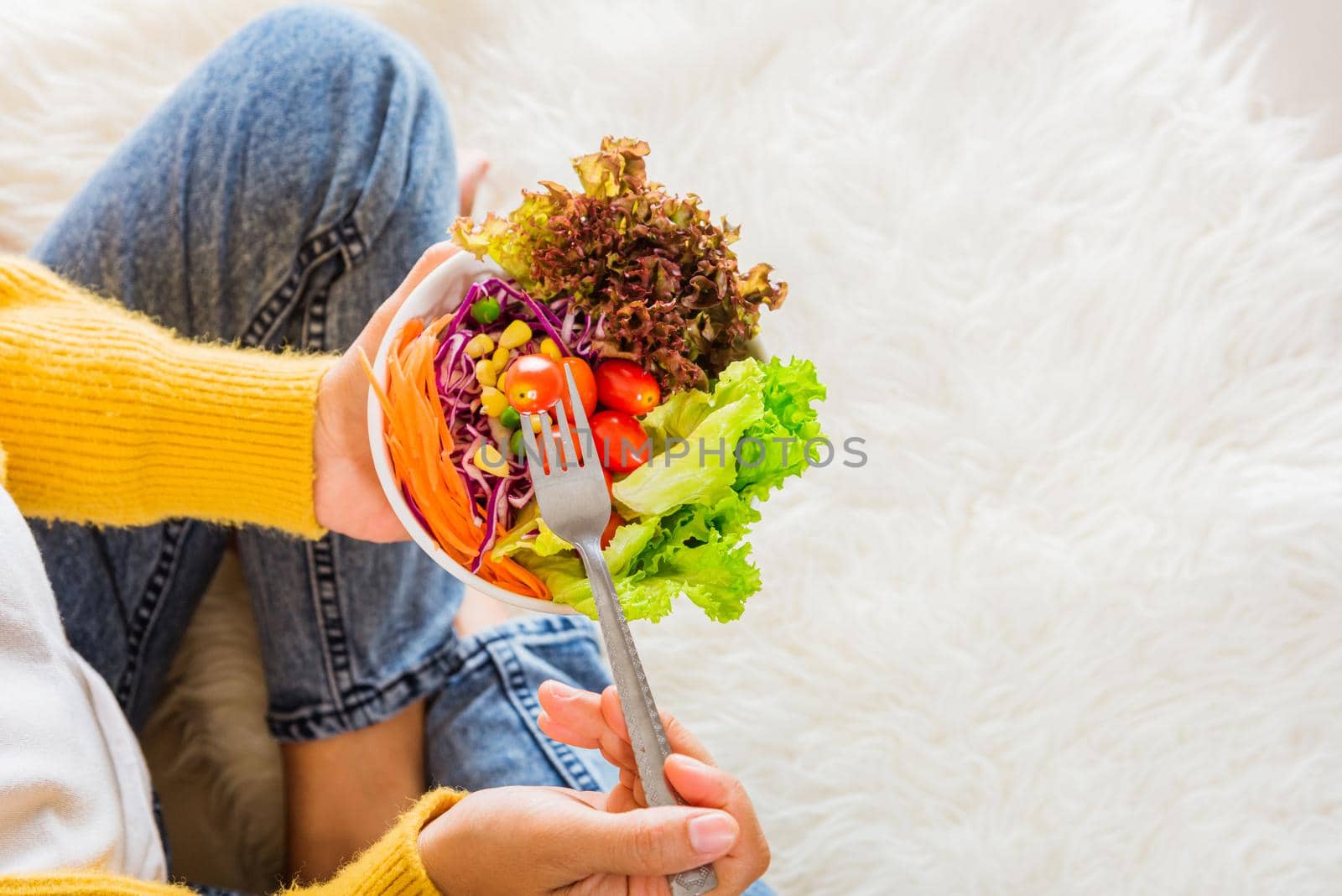 Top view of female hands holding bowl with green lettuce salad on legs, a young woman eating fresh salad meal vegetarian spinach in a bowl, Clean detox healthy food concept