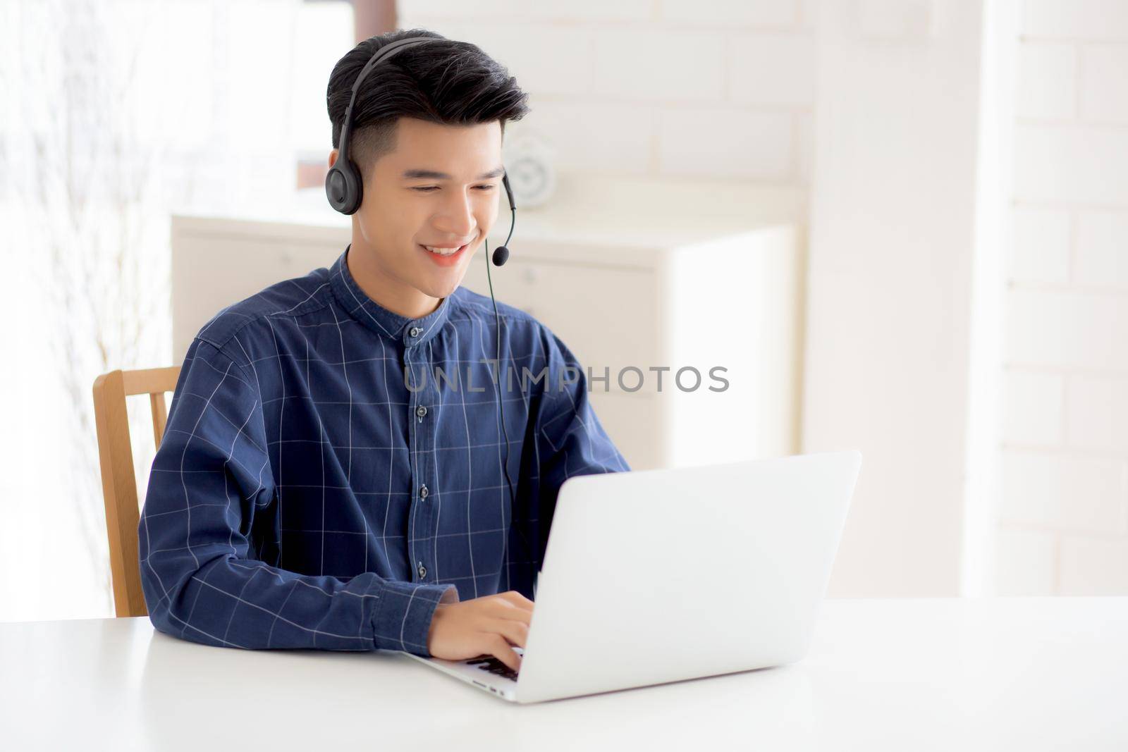 Young asian businessman working on laptop computer wearing headphone at home, business man wearing headset for video conference, communication and education, male study and learning for e-learning.