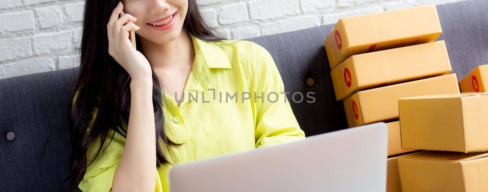 Young asian woman is entrepreneur talking with customer and using laptop computer while order purchase online at home, logistic and delivery, online shopping, female is seller of business SME. by nnudoo