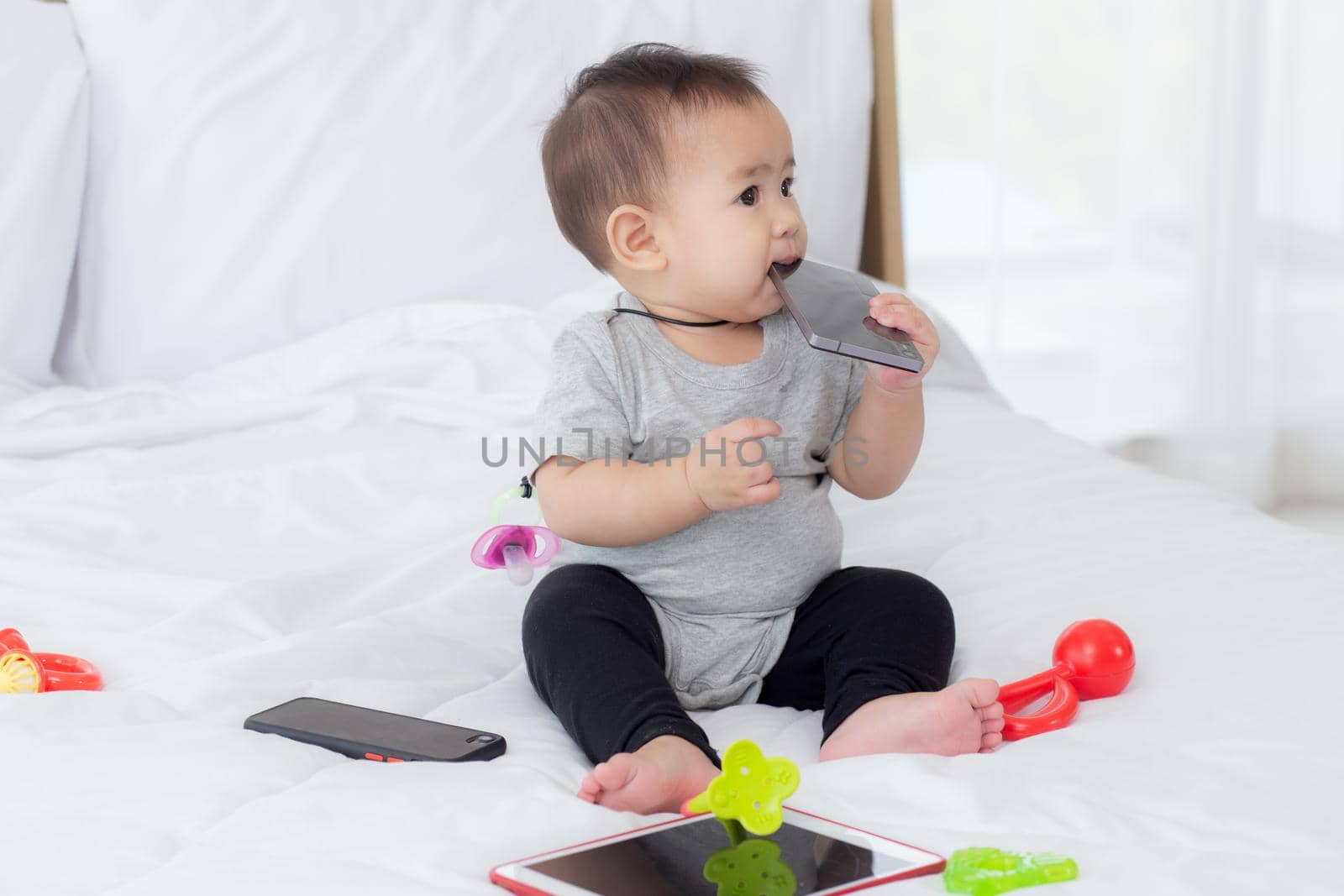 Portrait of cute little baby girl sitting with cozy on bed at bedroom, happiness of toddler, newborn 6-11 months with innocence and expression with cheerful, child charm, indoors, one person.