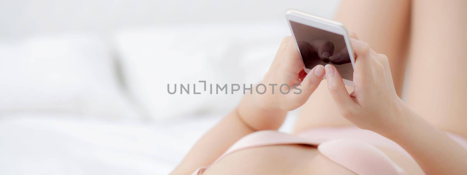 Young asian woman sexy in underwear chatting on mobile phone in the bedroom, girl in lingerie looking social media on smartphone lying on bed, communication and lifestyle concept, banner website.