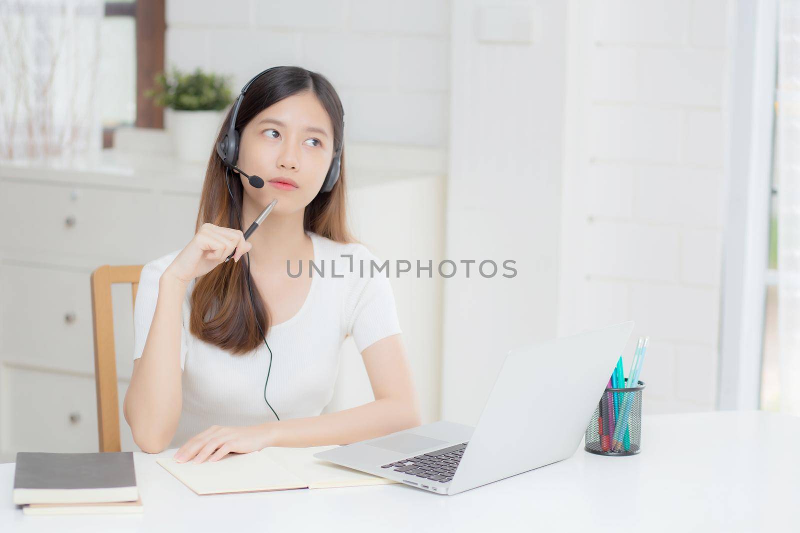 Young asian woman wearing headphone study online with e-learning on desk, girl wearing headset learning to internet with laptop computer at home, new normal, distance education and training.