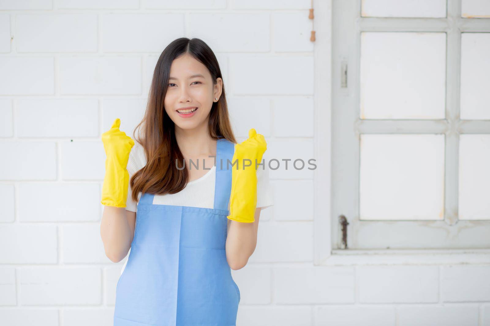 Portrait young asian woman is housekeeper in rubber gloves and apron for protection at home, uniform of maid, cleaning and washing, girl standing worker positive, one people, lifestyle concept.