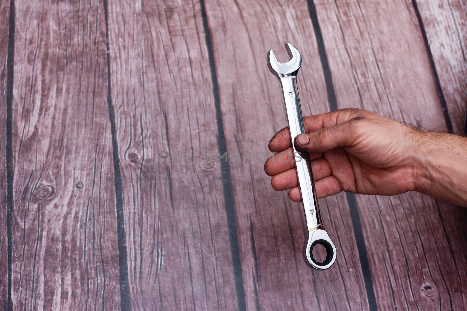 a wrench with ratchet in a man's hand. On a wooden background. My hand is smeared with work. 