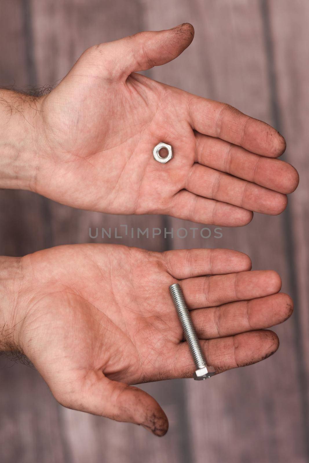Bolt and nut in men's hands on a wooden background. Close-up. The worker's hands are dirty.