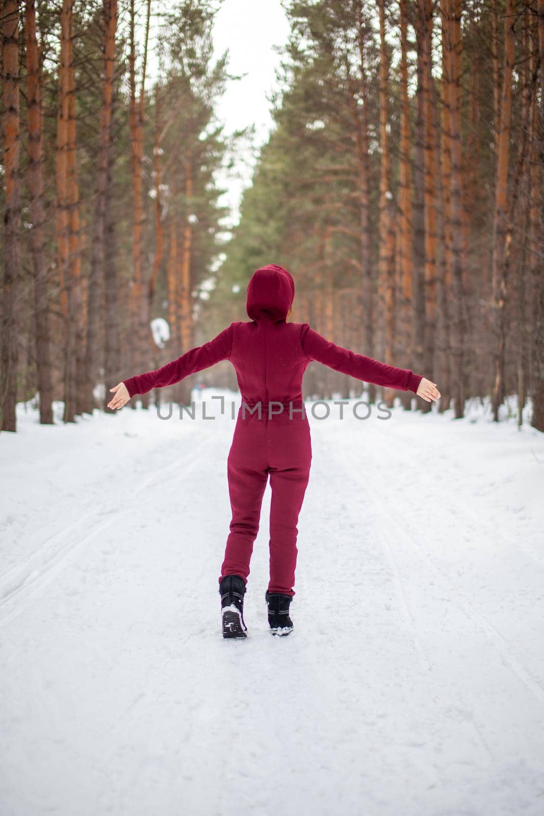 Winter walk in a snow-covered forest, A girl with a red jumpsuit and jacket walks among tall trees in nature. Solitude and relaxation from the hustle and bustle of the city.