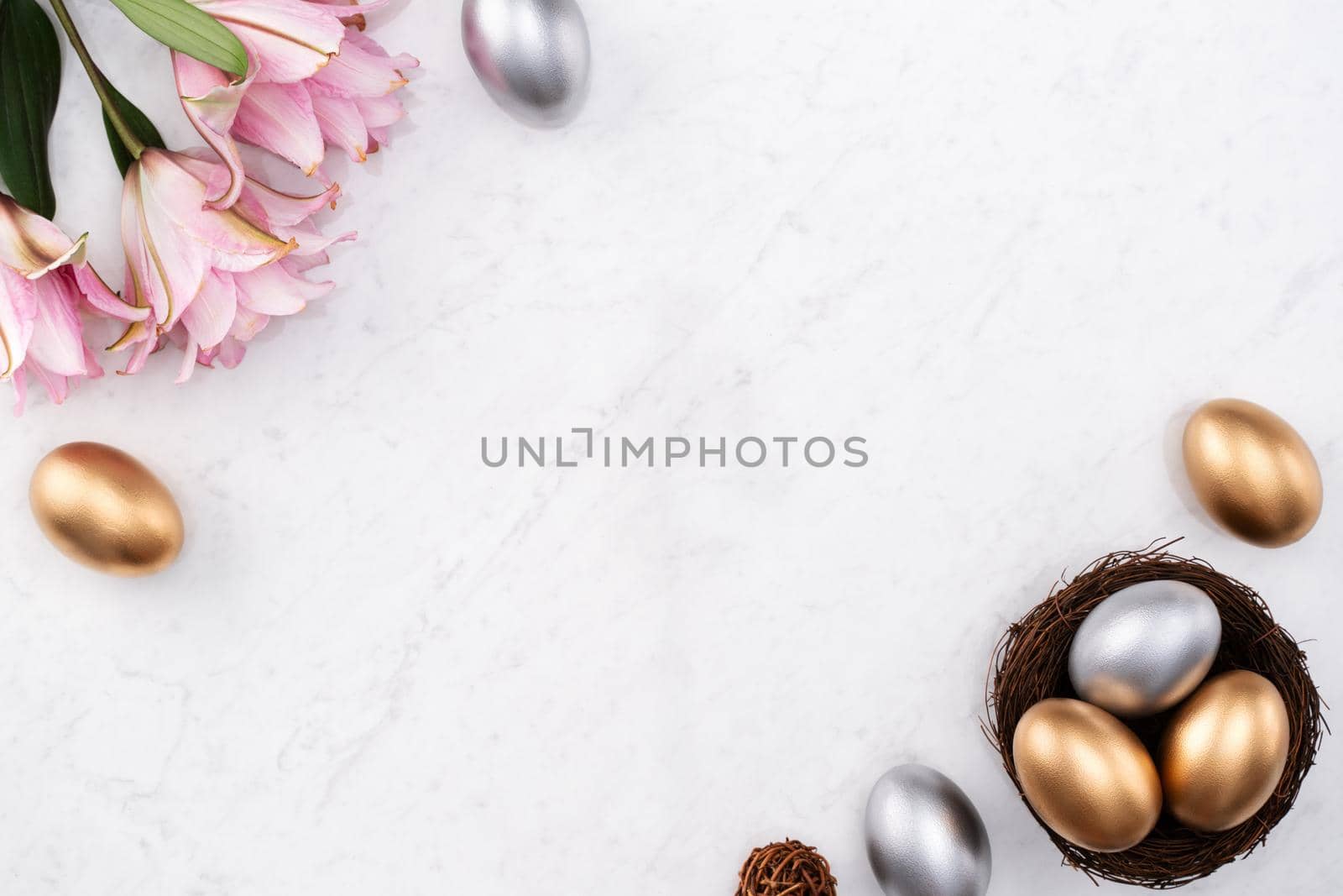 Design concept of Golden and silver Easter eggs in the nest with pink lily flower on bright marble white table background.