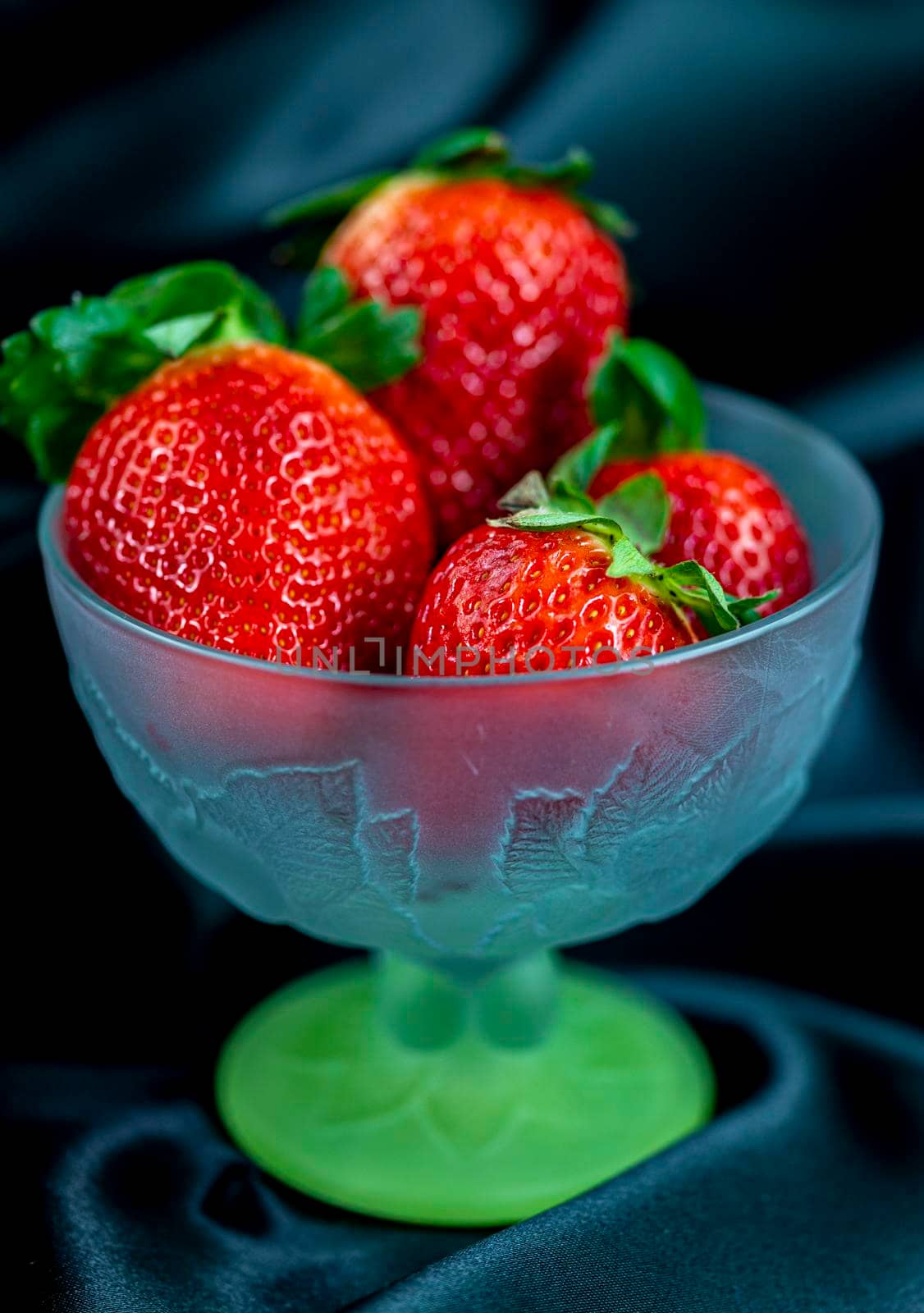 cup of ripe strawberries on black satin fabric background