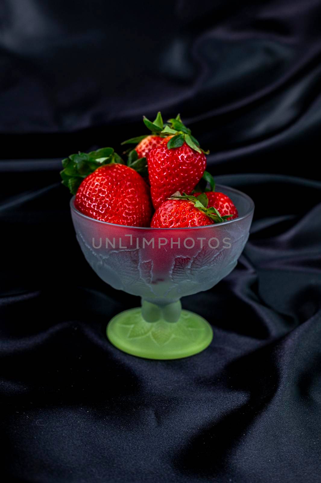 cup of ripe strawberries on black satin fabric background