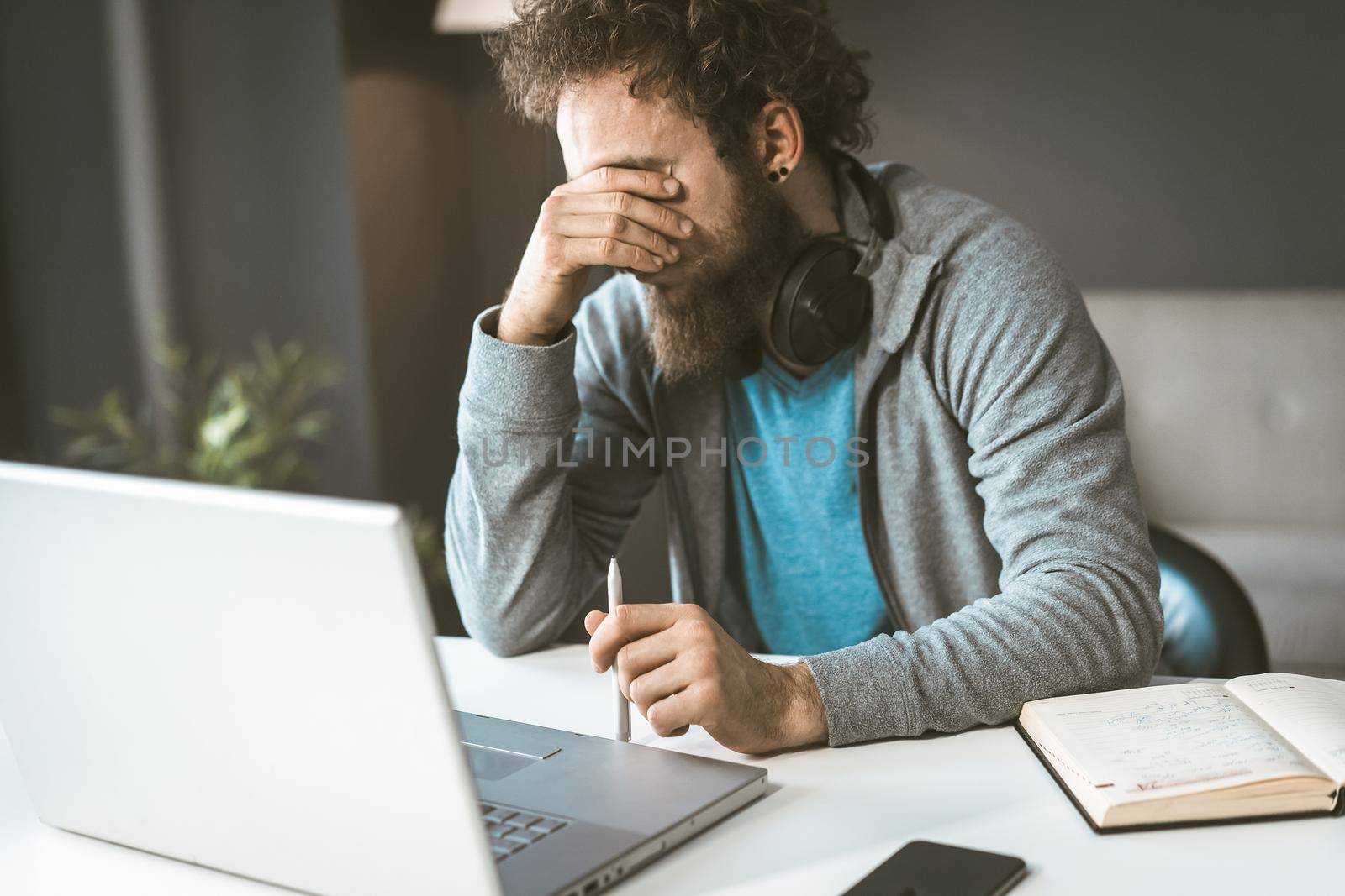 Facepalm. Crisis in business. A sad man sits in the workplace covering his face with his hand. by LipikStockMedia