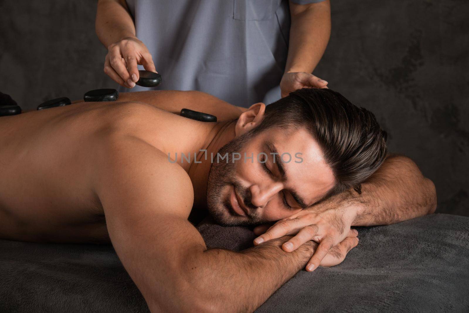 A good-looking man getting hot stone massage lying down at spa