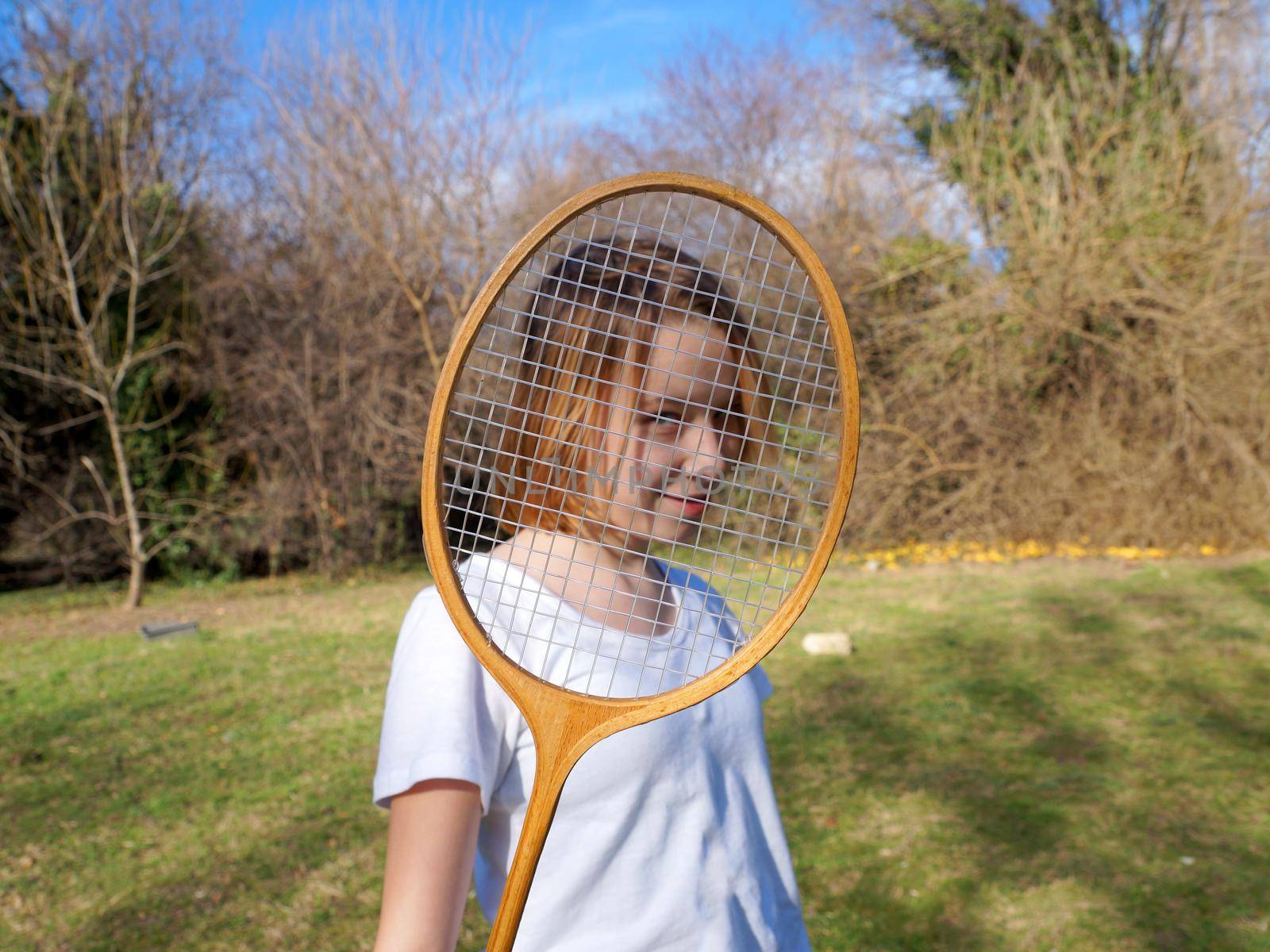 teenage girl looking through badminton racket and smiling by Annado